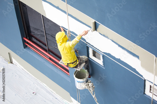 painters hanging on roll, painting color on building wall.