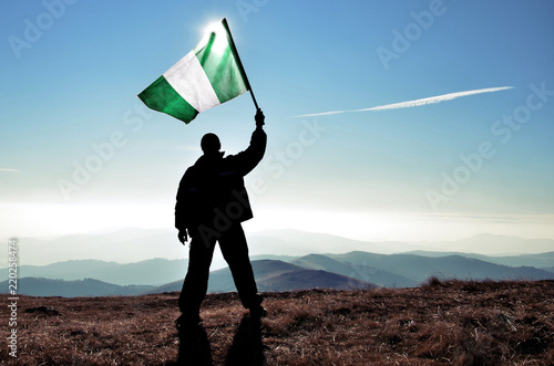Canvas Print Successful silhouette man winner waving Nigeria flag on top of the mountain peak