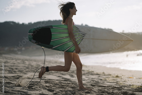 Woman with surfboard standing on wet sandy beach at the ocean.