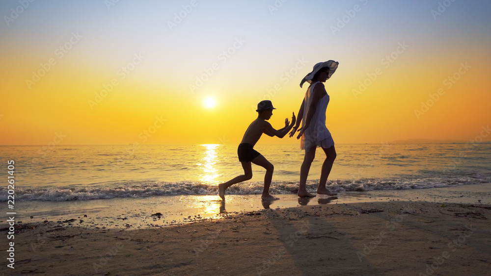 Tourism and travel vacation. Adorable family having fun on beach against sunset. Mother and son walk on beach an play, cinematic steadicam shot