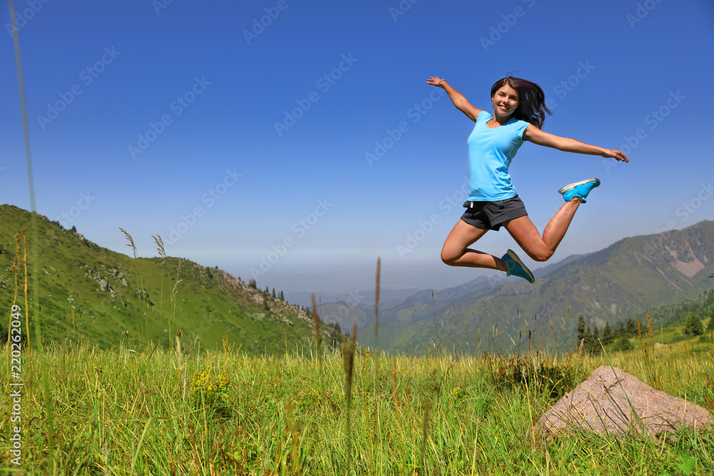 Happy joyful girl jumping against the blue sun and mountains Happy joyful girl jumping against the blue sun and mountains