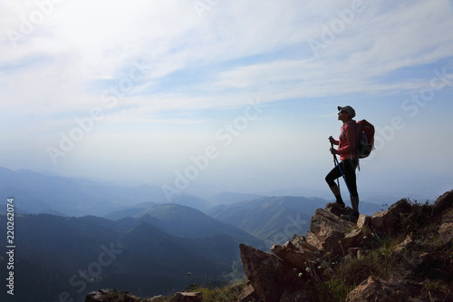 Lady hiker with backpack standing on top of the mountain