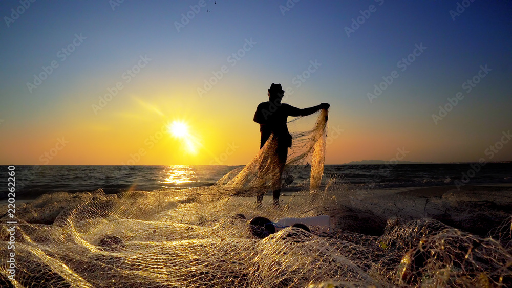 Silhouette of traditional fishermens pulling net fishing at ocean coast at sunset - obrazy, fototapety, plakaty 