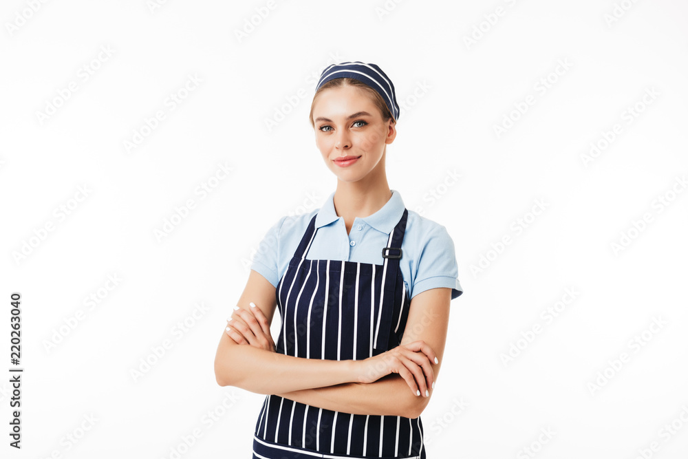 Beautiful woman cook in striped apron and cap dreamily looking in camera with arms folded over white background Beautiful woman cook in striped apron and cap dreamily looking in camera with arms folded over white background