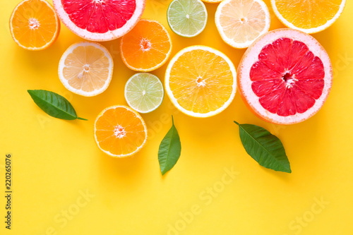 Fototapeta Kreatywne tło z letnich owoców tropikalnych z liśćmi, grejpfrut, pomarańcza, mandarynka, cytryna, limonka na pastelowym żółtym tle. Koncepcja żywności. Płaski układanie, widok z góry, kopia przestrzeń