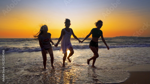 Group of female friends having fun running down the beach at sunset  cinematic steadicam traking shot