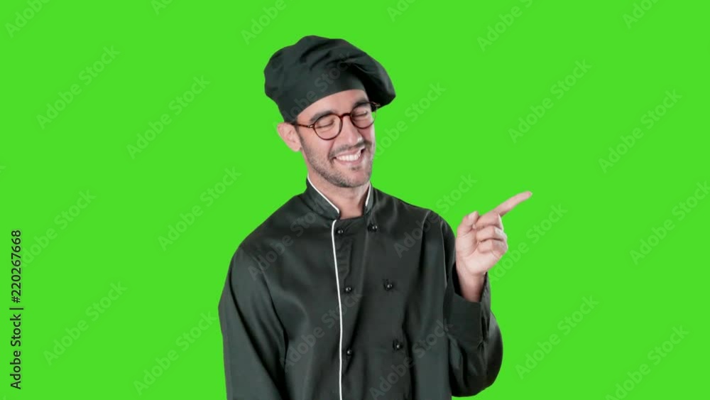 Happy young chef pointing with his finger against green background Happy young chef pointing with his finger against green background