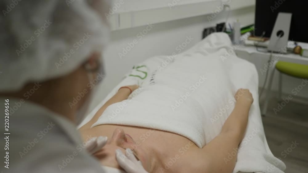 Beautician in medical gloves makes face massage with moisturizing cream for relaxed woman Beautician in medical gloves makes face massage with moisturizing cream for relaxed woman