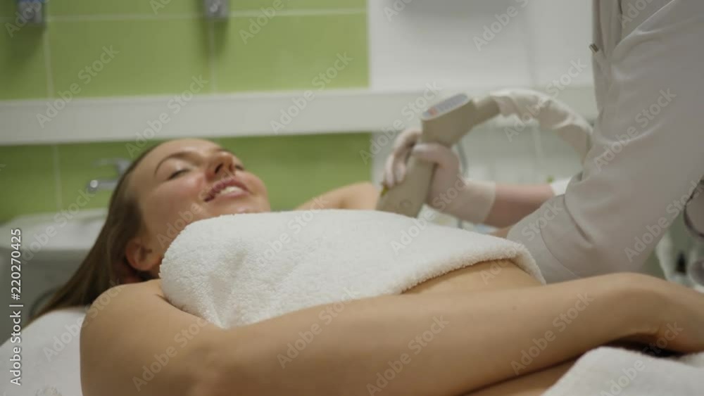 Smiling woman on couch gets cosmetology treatment with professional equipment Smiling woman on couch gets cosmetology treatment with professional equipment