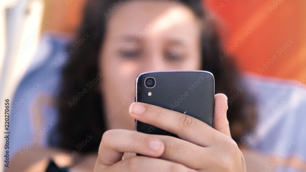 Female teen play games on smartphone during summer holidays lying on beach bed, cinematic selective focus dof Female teen play games on smartphone during summer holidays lying on beach bed, cinematic selective focus dof