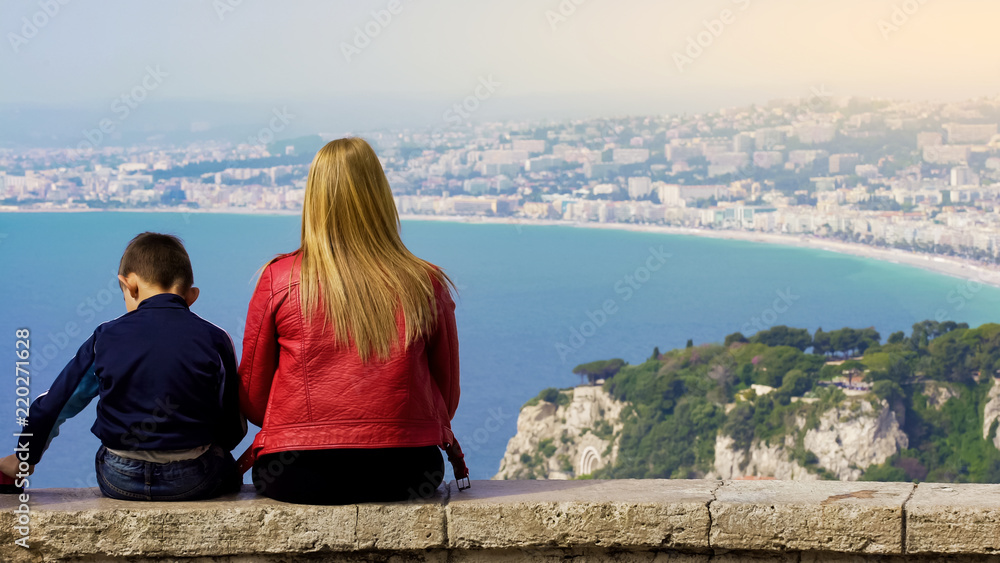 Mother and little son sitting on stone bench and enjoying fantastic view of city