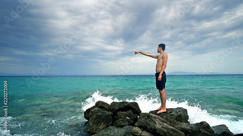 Lost alone male teen standing on sea rock and navigating horizon