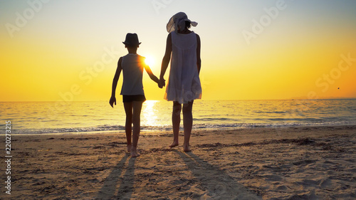 Family in love at summer sea sunset. Mother in white dress embrace little son with hat standing on empty beach