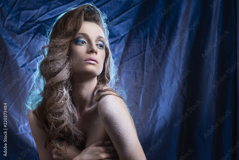 Beautiful young long-haired topless model girl with snow-covered skin and  hair covers her big breasts with her hands on a blue crumpled background  Stock Photo | Adobe Stock