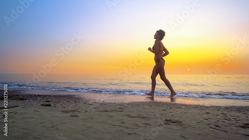 Barefoot sport woman in bikini jogging  running on an empty beach at sunset
