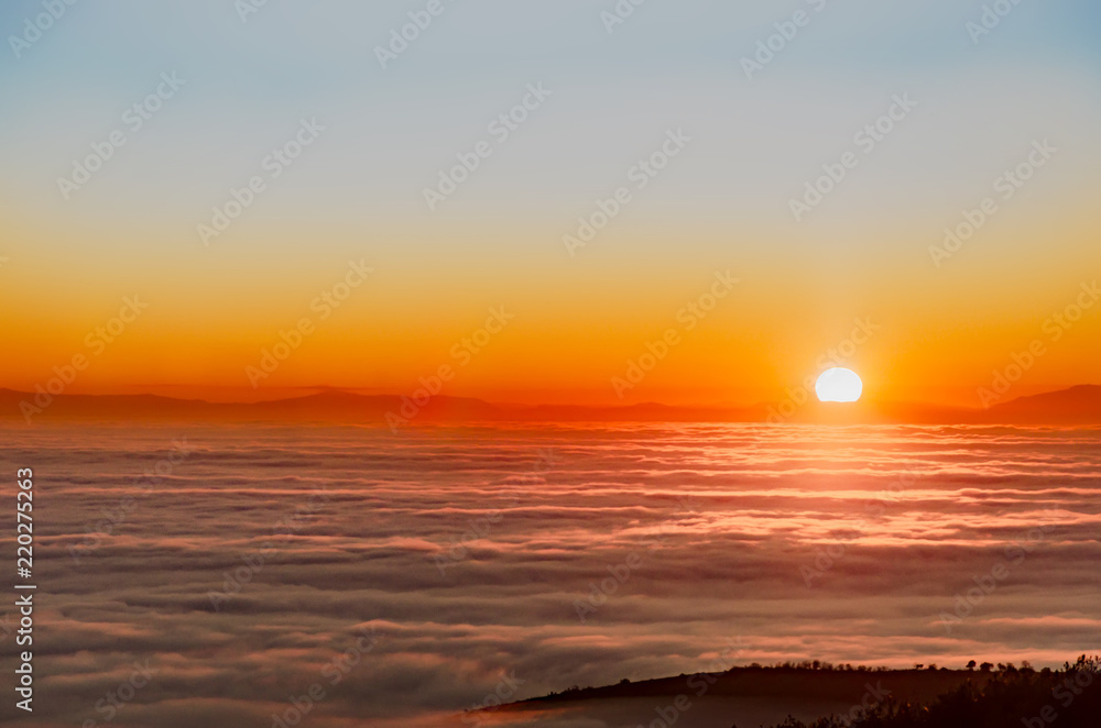 Beautiful misty sunset over mountain summit covvere3d with fog, aerial view, view on clouds from above, bright sun