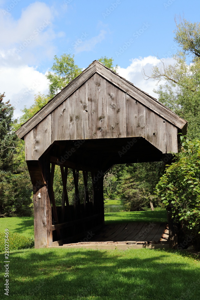 Vertical shot of an old wooden covered bridge with blue sky and fluffy white clouds