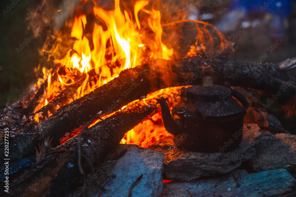 Boiling of tea in kettle on bonfire with large firewood. Tea drinking in open air. Active outdoor recreation. Camping in dusk. Romantic warm atmosphere in twilight on nature. Active rest. Boiling of tea in kettle on bonfire with large firewood. Tea drinking in open air. Active outdoor recreation. Camping in dusk. Romantic warm atmosphere in twilight on nature. Active rest.