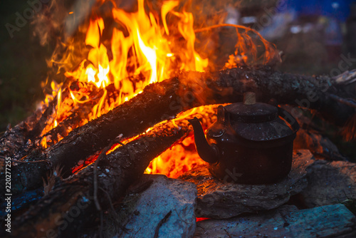 Boiling of tea in kettle on bonfire with large firewood. Tea drinking in open air. Active outdoor recreation. Camping in dusk. Romantic warm atmosphere in twilight on nature. Active rest.