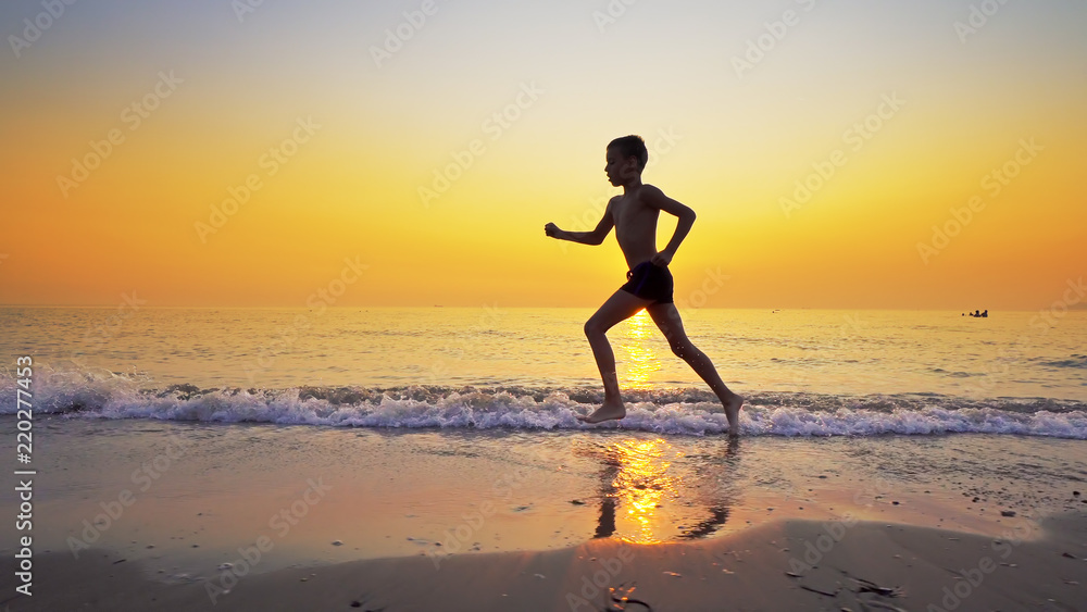 Sport boy running on sea beach against sunset at background