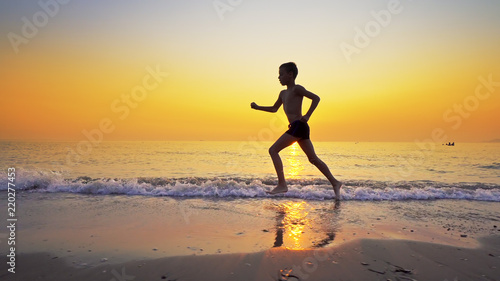 Sport boy running on sea beach against sunset at background
