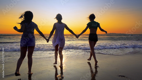 Young women and two girls run out of ocean water at sunset on tropical beach. Cinematic steadicam