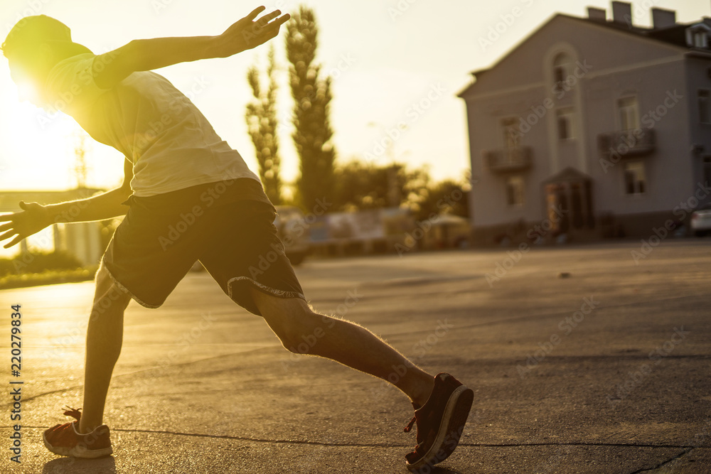 back view of young man athlete in casual silhouette running in the urban city on a sunset