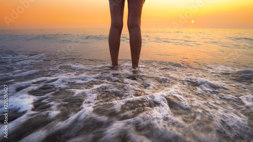 Woman feet splashed by sea waves on beach sunset. Calm serene relaxing scene of ocean water splashing on feet on beautiful beach
