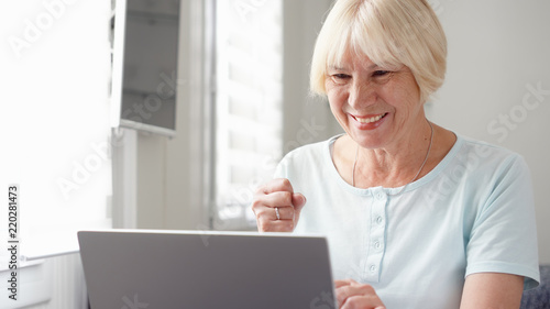 Elderly senior blond woman working on laptop computer at home. Received good news excited and happy. Remote freelance work on retirement, active modern lifestyle of older people. Success concept
