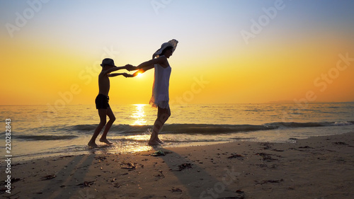 Tourism and travel vacation. Adorable family having fun on beach against sunset. Mother and son walk on beach an play, cinematic steadicam shot