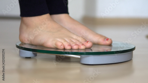 Female bare feet with weight scale on wooden floor, weight loss diet
