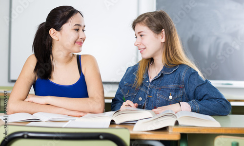 Two girls are sitting at the desk and writing homework