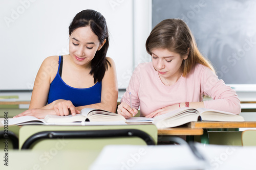 Two girls are sitting at the desk and writing homework © JackF