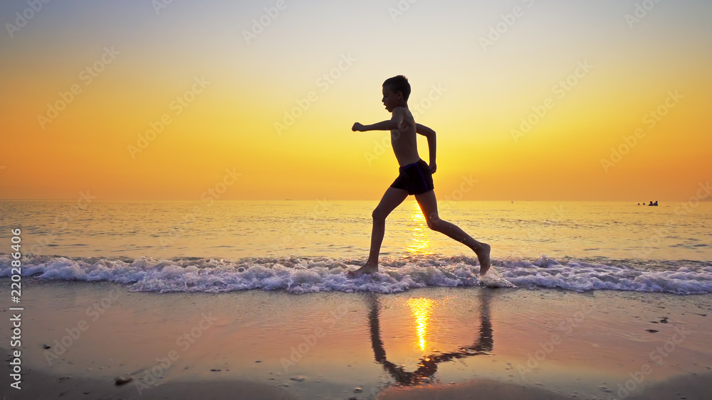 Sport boy running on sea beach against sunset at background