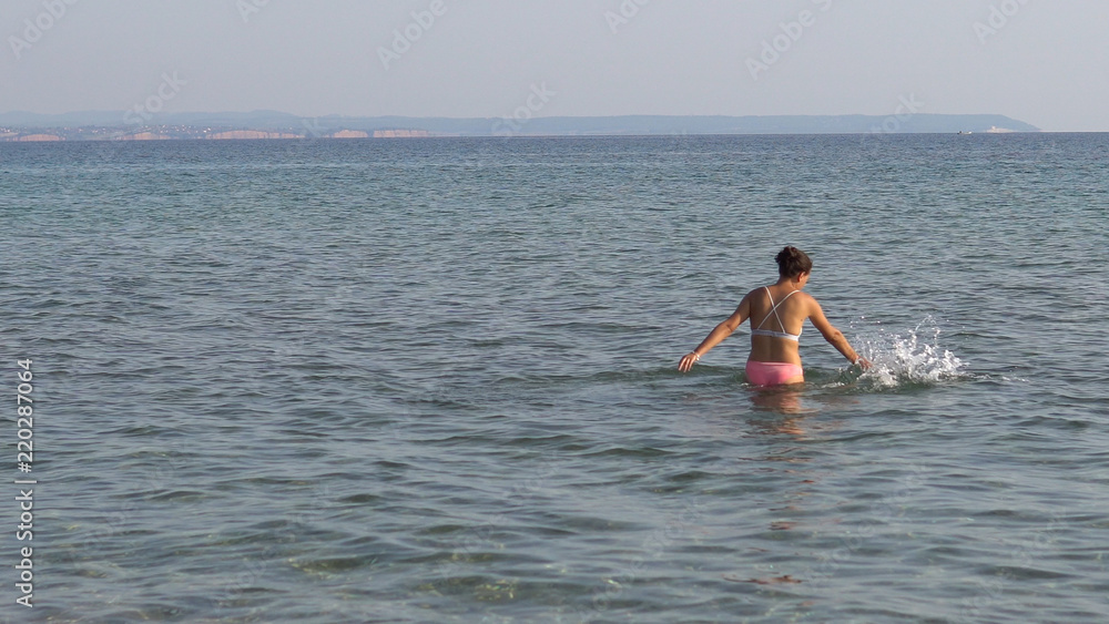 Lonely young woman plays alone in sea shallow water splashing with her hands