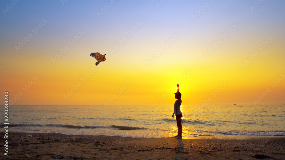 Boy launch a kite running on beach at sunset, cinematic steadicam shot