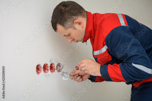 Electrician hands tighten electrical wires in wall fixture or socket using a screw driver - closeup. Installing electrical outlet or socket - closeup on electrician hands photo