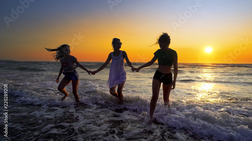 Silhouettes of young group of people jumping in ocean at sunset, cinemati shot.Concept of friendly family.