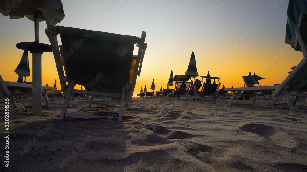 Travel concept. The low season. All umbrellas are close on the beach against sunset. The period in the year when the fewest people visit a place and when the prices are at their lowest level