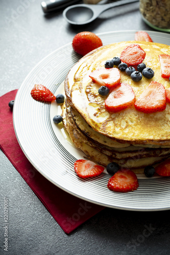 Sweet pancakes with honey, strawberries, and blueberry on a modern white plate. 