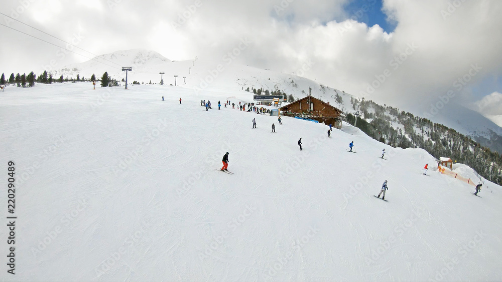 Aerial view from ski lift to ski piste with strong wind and snow drifting at the top of mountain summit, slow motion