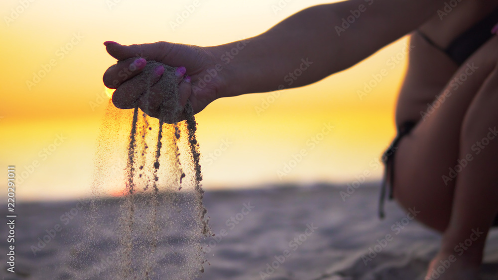 Sand slips through female fingers on beach against sea sunset. Concept