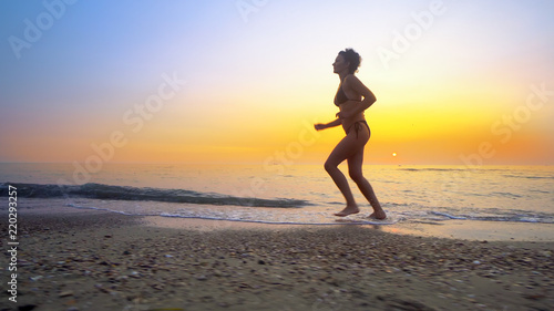 Barefoot sport woman in bikini jogging  running on an empty beach at sunset