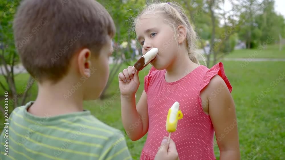 little girl and boy children are eating ice cream in a park in summer day, standing on a grass little girl and boy children are eating ice cream in a park in summer day, standing on a grass