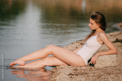 Beautiful young sexy girl in a swimsuit sunbathing on the beach, lying by the sea, leaning on a stone