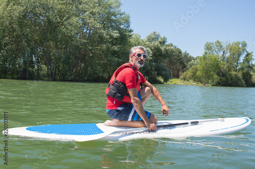 mature attractive rider contemplating nature sitting on paddle board