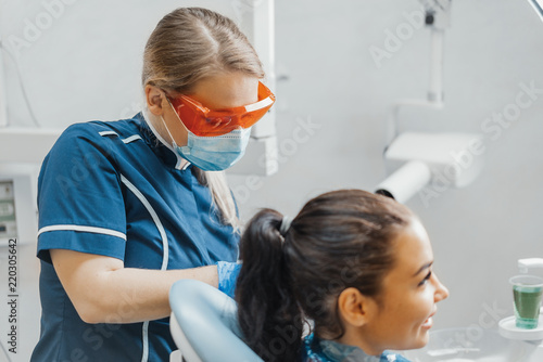 Close up of woman dentist putting on plastic apron on smiling woman client.
