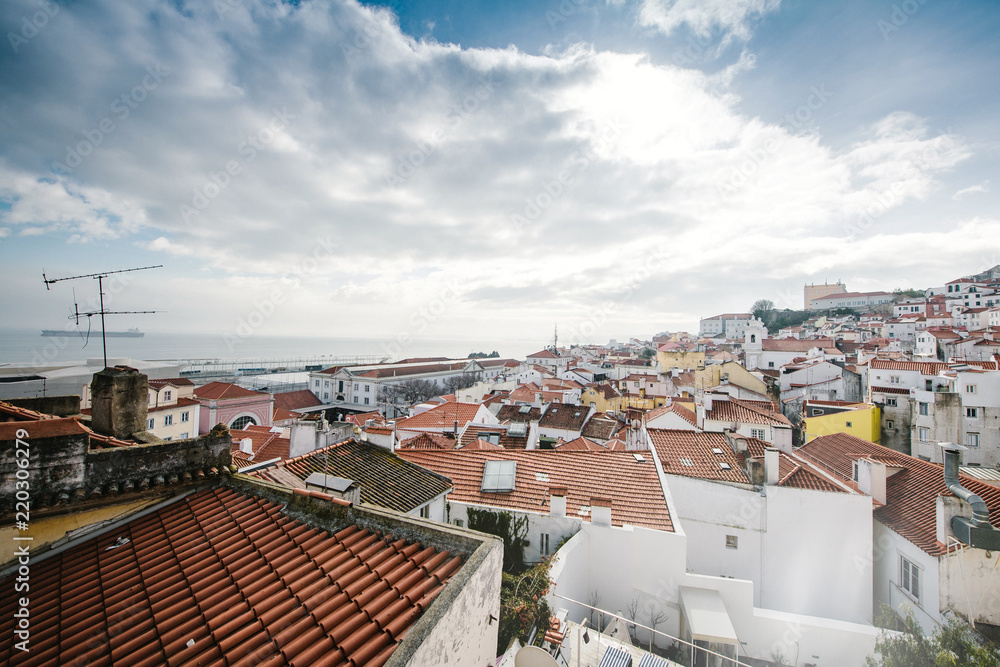 Aerial shot of city of Lisbon with colorful rooftops in sunlight with cloudy sky and calm ocean Portugal Lisbon