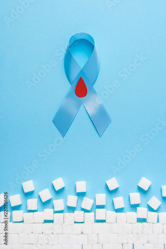 blue ribbon awareness with red blood drop and ruined wall made of sugar cubes on a blue background, world diabetes day