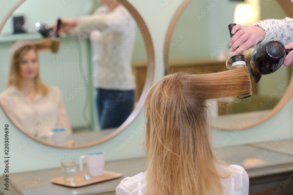 hairstylist using a curling iron of a female client hairstylist using a curling iron of a female client